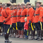 RCMP members in scarlet on parade with a young boy in RCMP costume posing with them.