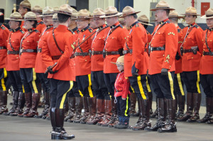 RCMP members in scarlet on parade with a young boy in RCMP costume posing with them.