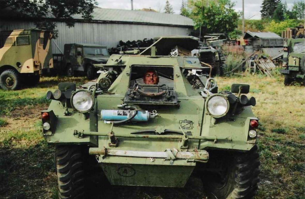 Man sitting in driver's seat of a Ferret Scout Car and looking out through the front hatch.