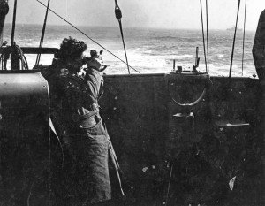 Naval officer in duffelcoat on bridge of ship using a sextant. Sub-Lieutenant Barry Brissendon from Victoria, B.C. taking a navigation sighting on board HMCS Malpeque 1942-43 (AHS p53 05 )