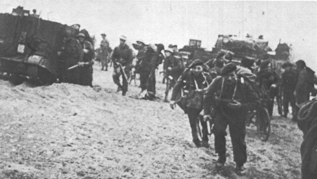 British Commando troops with BSA airborne bicycles passing a Universal Carrier on the beach in Normandy. 