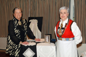 Two ladies. One on right in Norwegian folk costume.