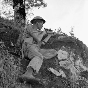 Sniper with helmet and No. 4 MK. I sniper rifle on a hiillside. 1943-10-06 Pte. J. E. (sic) McPhee, a sniper with the Seaforth Highlanders of Canada near Foiano, Italy. The only McPHEE was K74808 Pte. McPHEE, F. J. who served with the Seaforths 21 Aug. 1942 - 26 Dec. 1943. He was wounded 20 Jul. 1943 near Leonforte (West of Mt. Etna), Sicily and was Killed in Action 26 Dec. 1943 in or near Ortona, Italy. He was 23 years old and the husband of Mildred Ethel McPhee of Vancouver, British Columbia, Canada. He is buried in grave VIII. G. 2. Moro River Canadian War Cemetery. (L&AC MIKAN 3207117)