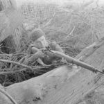 Soldier with rifle behind a large tree branch. 1942 approx Sniper in training in UK with P-14 with target sights. (L&AC MIKAN 3607526)