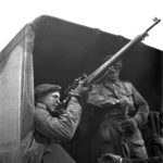 1943-04-23 Unidentified soldier sighting with his telescope equipped P-14 sniper rifle while sitting in the back of a 15 Cwt truck. 2 Canadian Infantry Division Sniper Training, England. Photo by Lieut. Grederick G. Whitcombe (L&AC PA-211643 MIKAN 3596210)