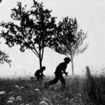 Two British WWII soldiers running among trees.