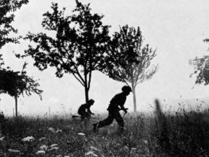 Two British WWII soldiers running among trees.