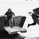 Brtiish soldier leaping off of a landing craft carrying his rifle.