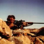 Sniper aiming his rifle. British Special Air Service (SAS) sniper in Oman in the 1970s with an L42A1 7.62mm sniper rifle. The cloth (groundsheet?) under the muzzle was likely to present the muzzle blast from stirring up a dust cloud which would reveal the sniper's position.