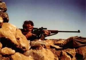 Sniper aiming his rifle. British Special Air Service (SAS) sniper in Oman in the 1970s with an L42A1 7.62mm sniper rifle. The cloth (groundsheet?) under the muzzle was likely to present the muzzle blast from stirring up a dust cloud which would reveal the sniper's position.