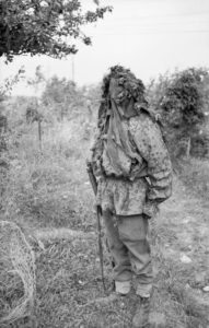 Sniper school camouflage demonstration. Man appears to be wearing a German camouflage jacket, so it may be instruction on recognizing the enemy sniper. Normandy 27 JUL 44 © IWM (B 8177)