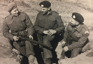 Three men talking with their feet in a trench with a sniper rifle.