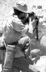 British sniper in Aden in 1964 aiming his No. 4 MK. I (T). He has a Case No. 8 MK. 2 slung to hold the No. 32 MK. 3 scope and its mounting bracket when they are not on the rifle. M1907 leather sling on the rifle. He has an unusual cartridge belt and he also has a clasp knife hanging down on the right side from a lanyard. (TMSS1914 p45)