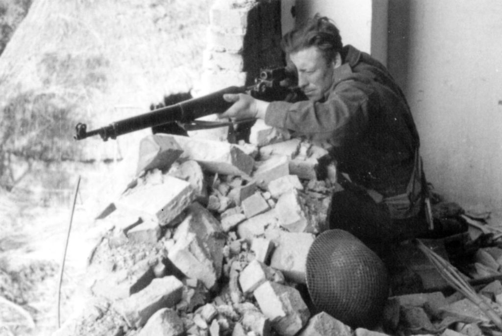 Sniper aiming his rifle from the rubble of a building.
