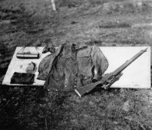 WWII British sniper's kit layout. Scout Regiment Telescope in case at top left; binoculars (top left as well; prismatic compass half out of pouch; General; Service watch (on cuff of smock); Camouflaged Denison smock and No. 4 (T) sniper rifle with No. 32 telescope fitted. WBSTTR - Shore 1948 fp 102