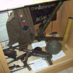 Case 6B - Major Alex "Sandy" Millar's CANLOAN BD blouse and framed CANLOAN scroll; two MP-40 SMGs, Italian helmet and two versions of the 2-INCH mortar. An Italian banner captured at AGIRA is behind them.