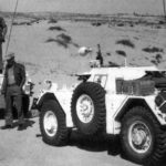 Two Ferret Scout Cars stopped in the desert. Men standing around.