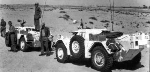 Two Ferret Scout Cars stopped in the desert. Men standing around.