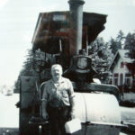 Man standing in front of a steam roller that he operated.