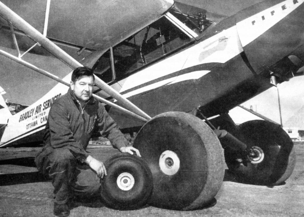 Man squatting beside small airplane with tires.