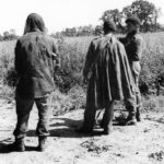 Three soldiers talking about a mission. They are standing and facing away from the camera.